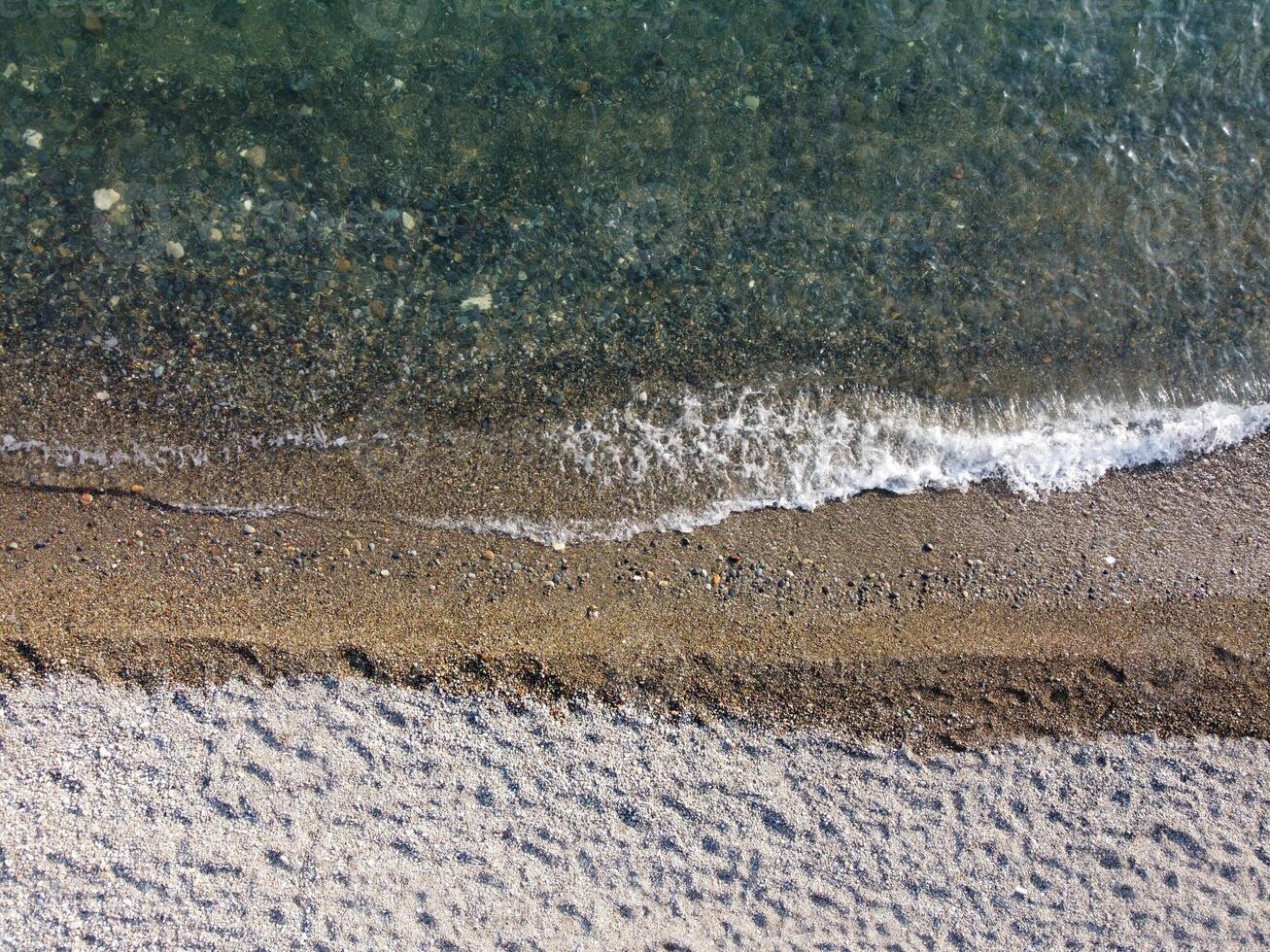 Aerial view from above on calm azure sea and pebbles beach. Small waves on cristal clear water surface in motion blur. Summer ocean sea beach background. Nobody. Holiday, vacation and travel concept photo