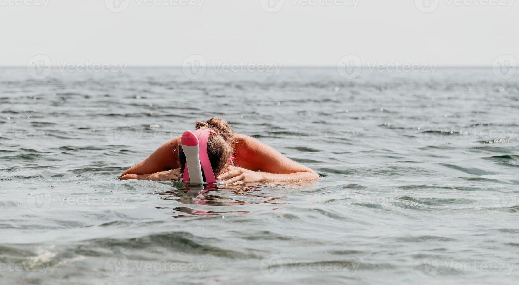 Young happy woman in white bikini and wearing pink mask gets ready for sea snorkeling. Positive smiling woman relaxing and enjoying water activities with family summer travel holidays vacation on sea. photo