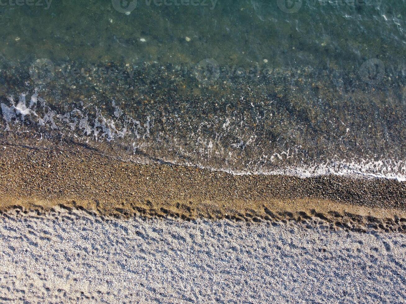 Aerial view from above on azure sea and pebbles beach. Small waves on cristal clear water surface in motion blur. Nature summer ocean sea beach background. Nobody. Holiday, vacation and travel concept photo