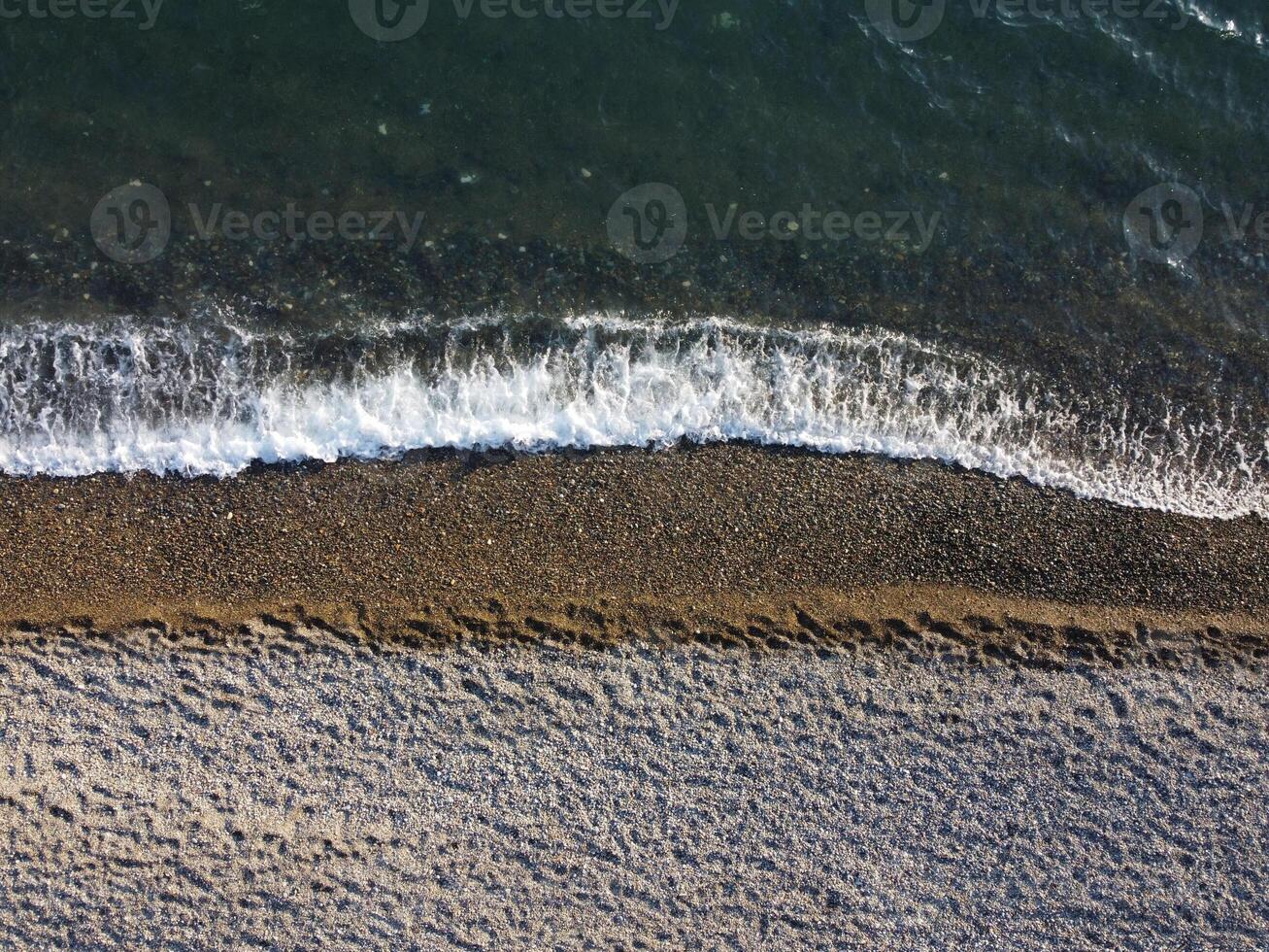 Aerial view from above on azure sea and pebbles beach. Small waves on cristal clear water surface in motion blur. Nature summer ocean sea beach background. Nobody. Holiday, vacation and travel concept photo