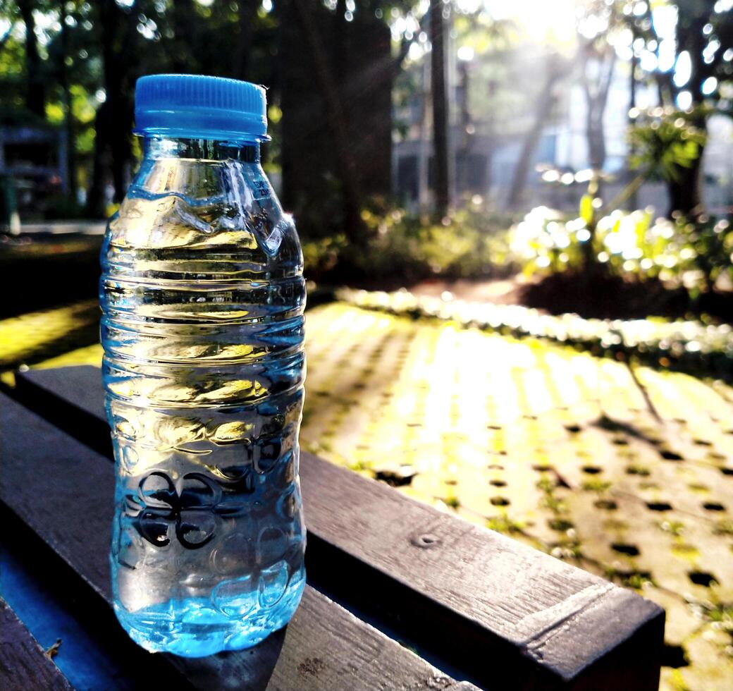 Plastic water bottle with blue label placed on a wooden table in the park in the morning with sunlight drop to the ground photo