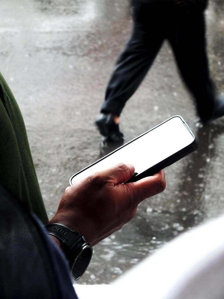 hand holding a smartphone with white blank screen on outdoor area during the rainy days photo