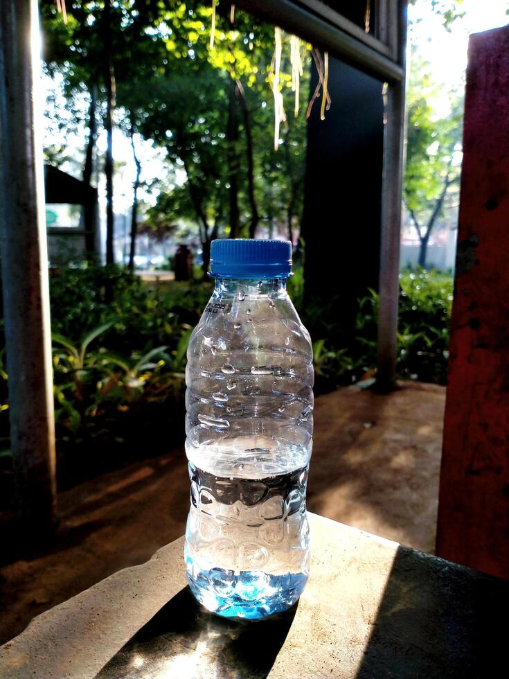 Plastic water bottle with blue label placed on a cement table in the park in the morning with sunlight drop to the ground photo