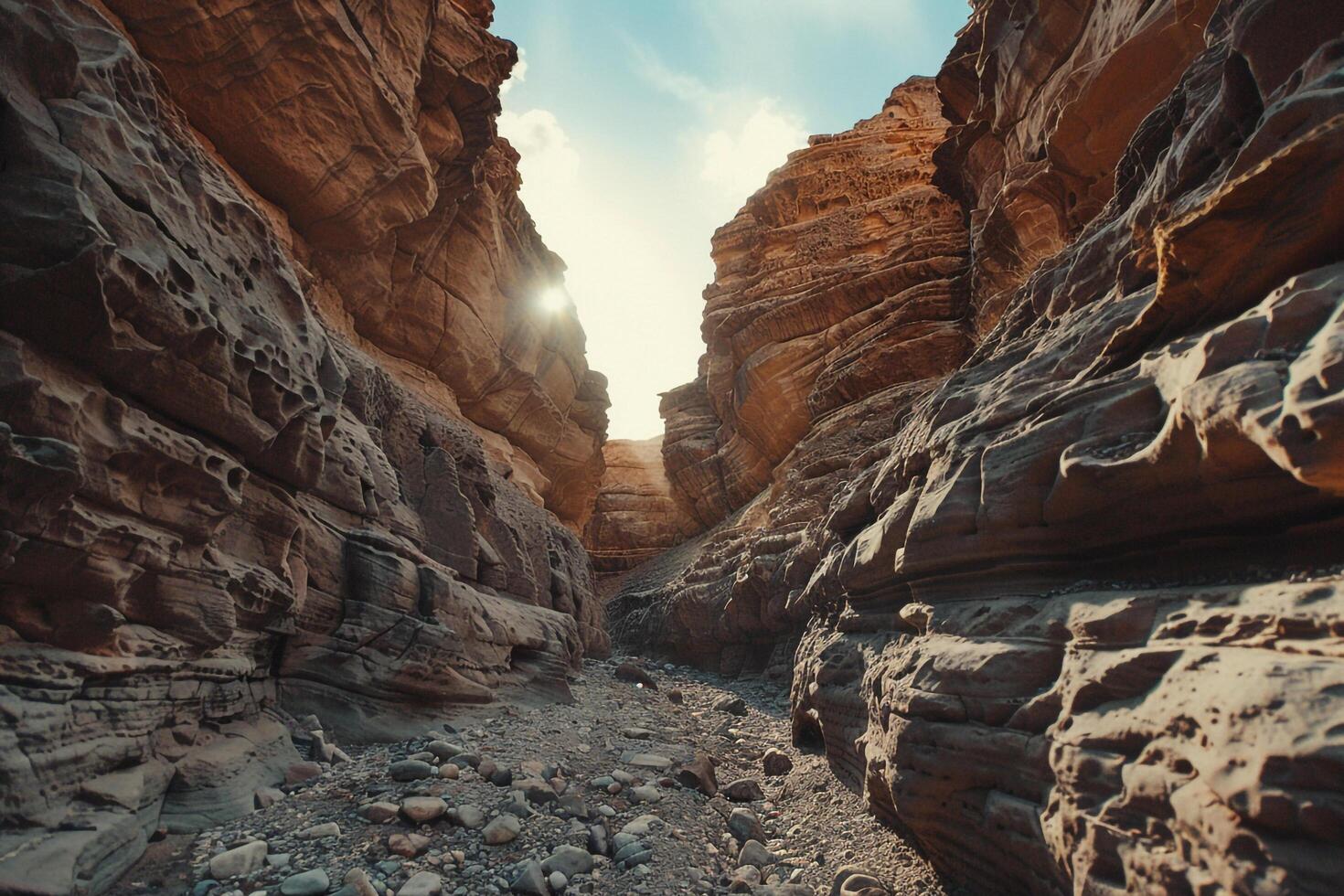 a narrow canyon with rocks and sun shining through background photo