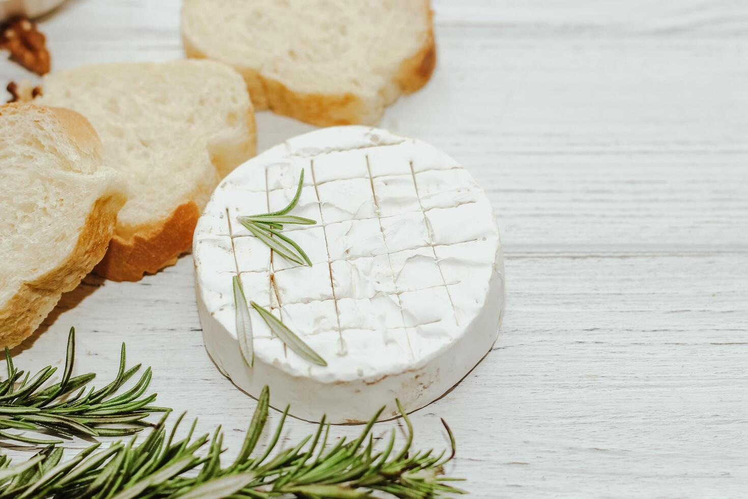Round cheese in camembert mold with a sprig of rosemary, honey and nuts on the table. photo