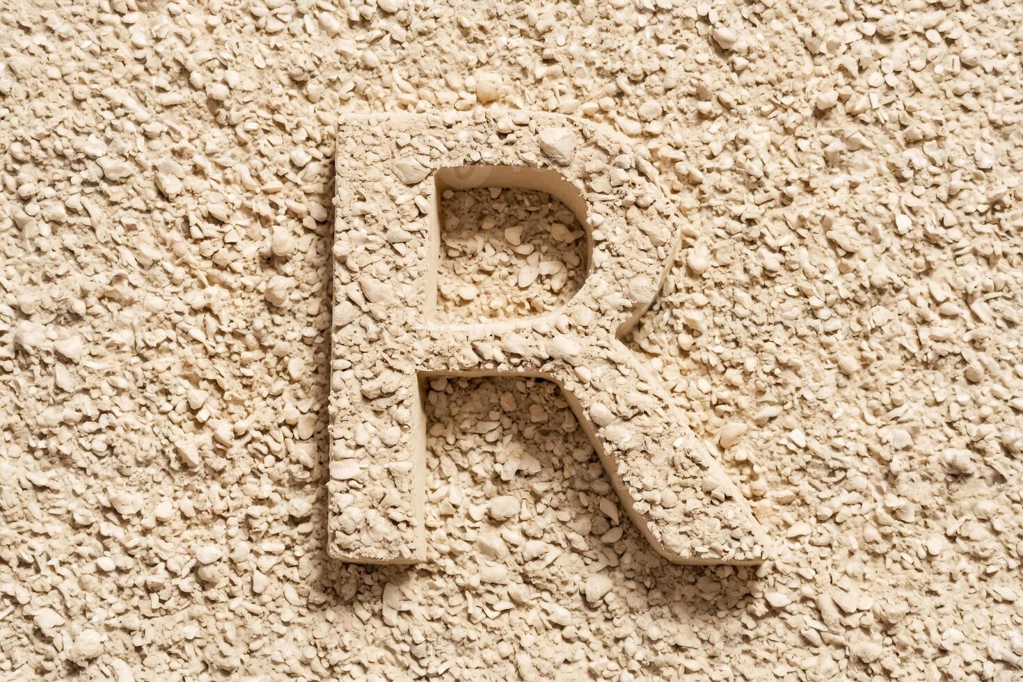 Letter R carved into a beige textured wall photo