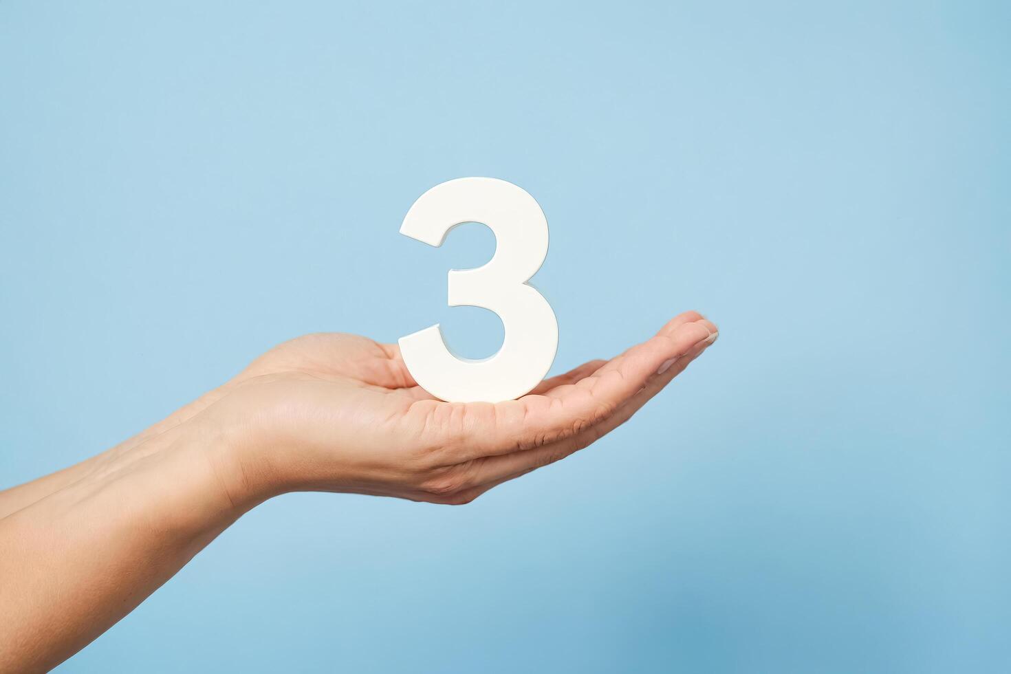 Number Three Held In Palm Of Hand On Blue Background photo