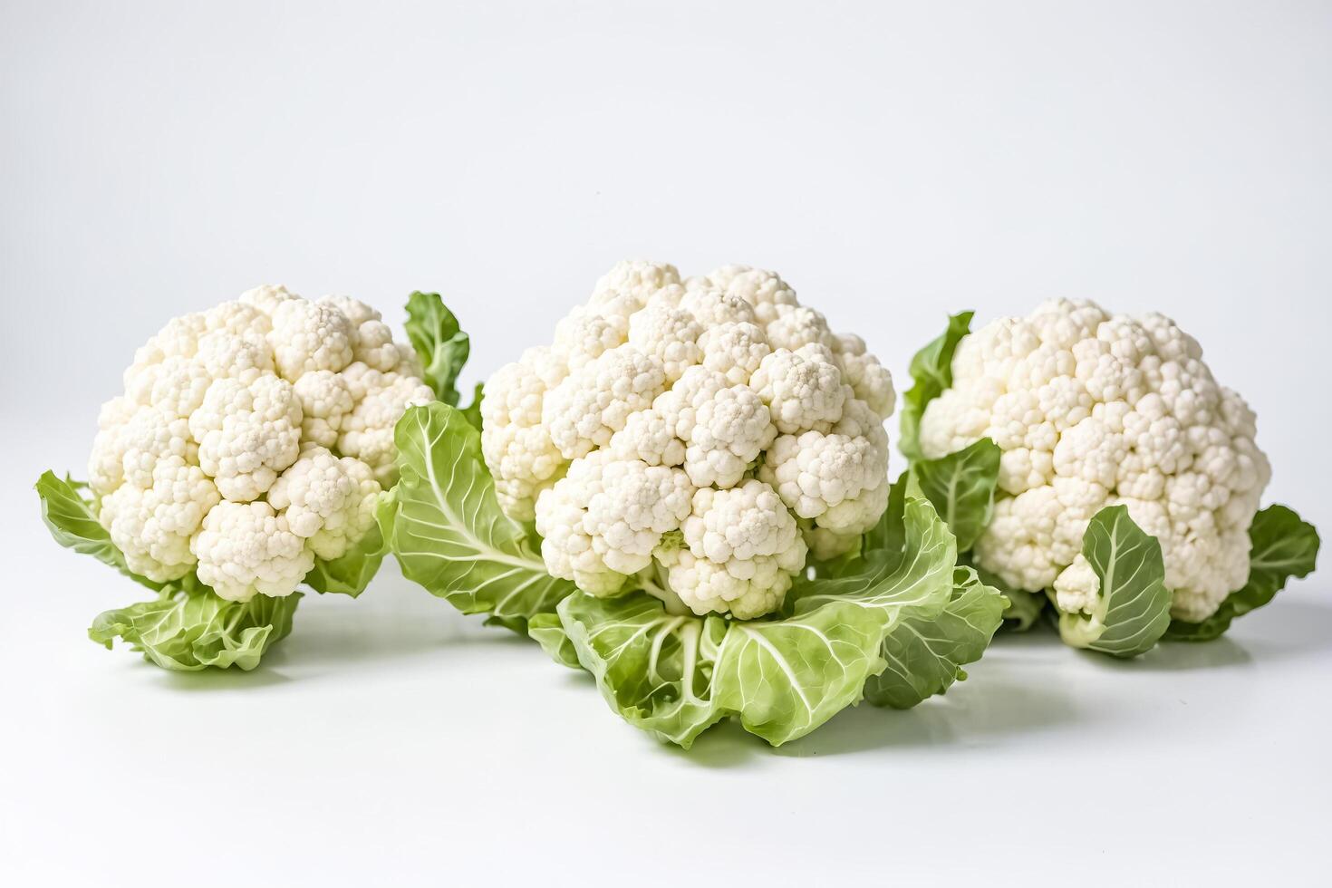 Three Fresh Caulifower Heads with Green Leaves photo