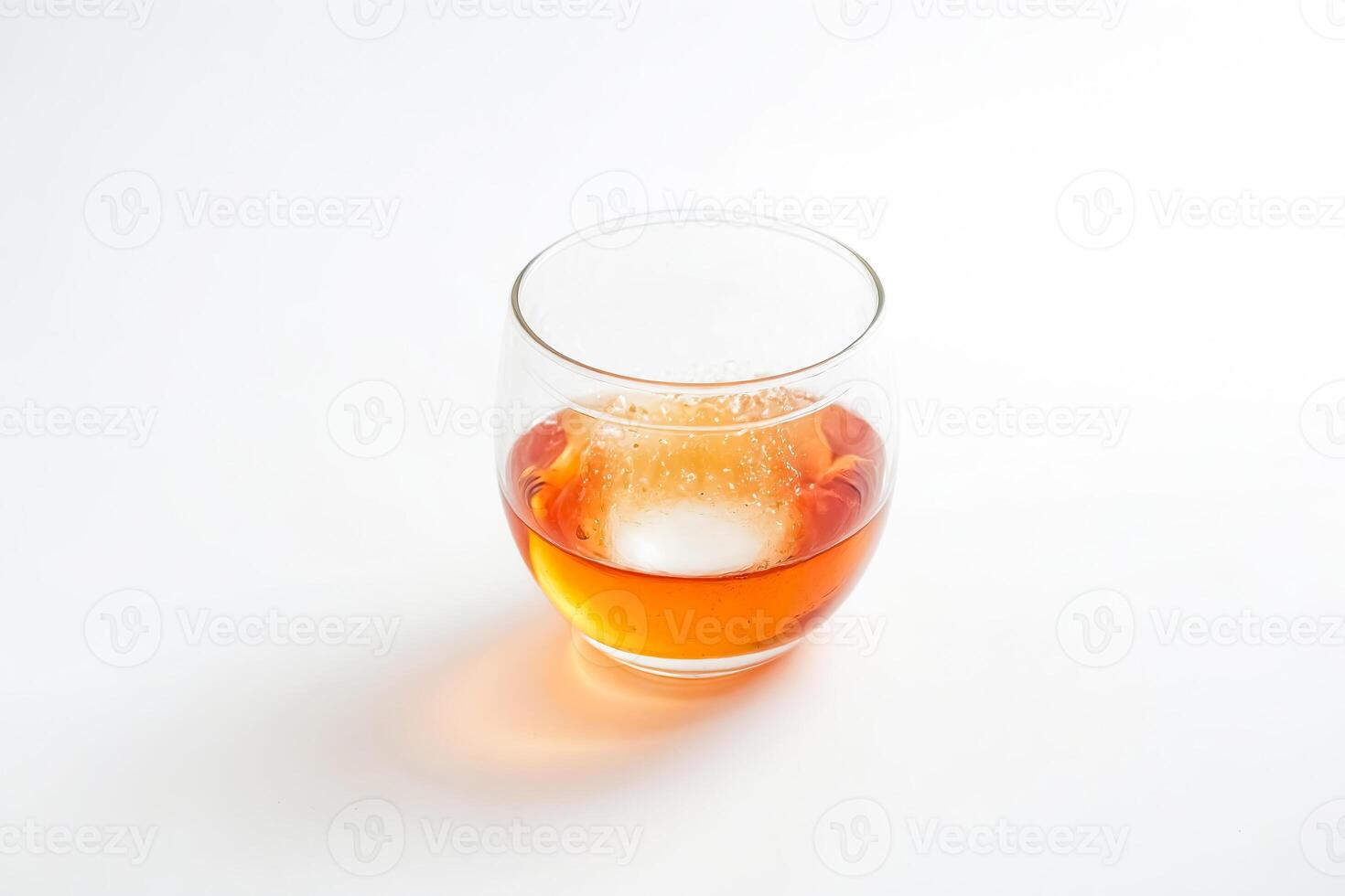 Glass of amber liquid with ice cube photo