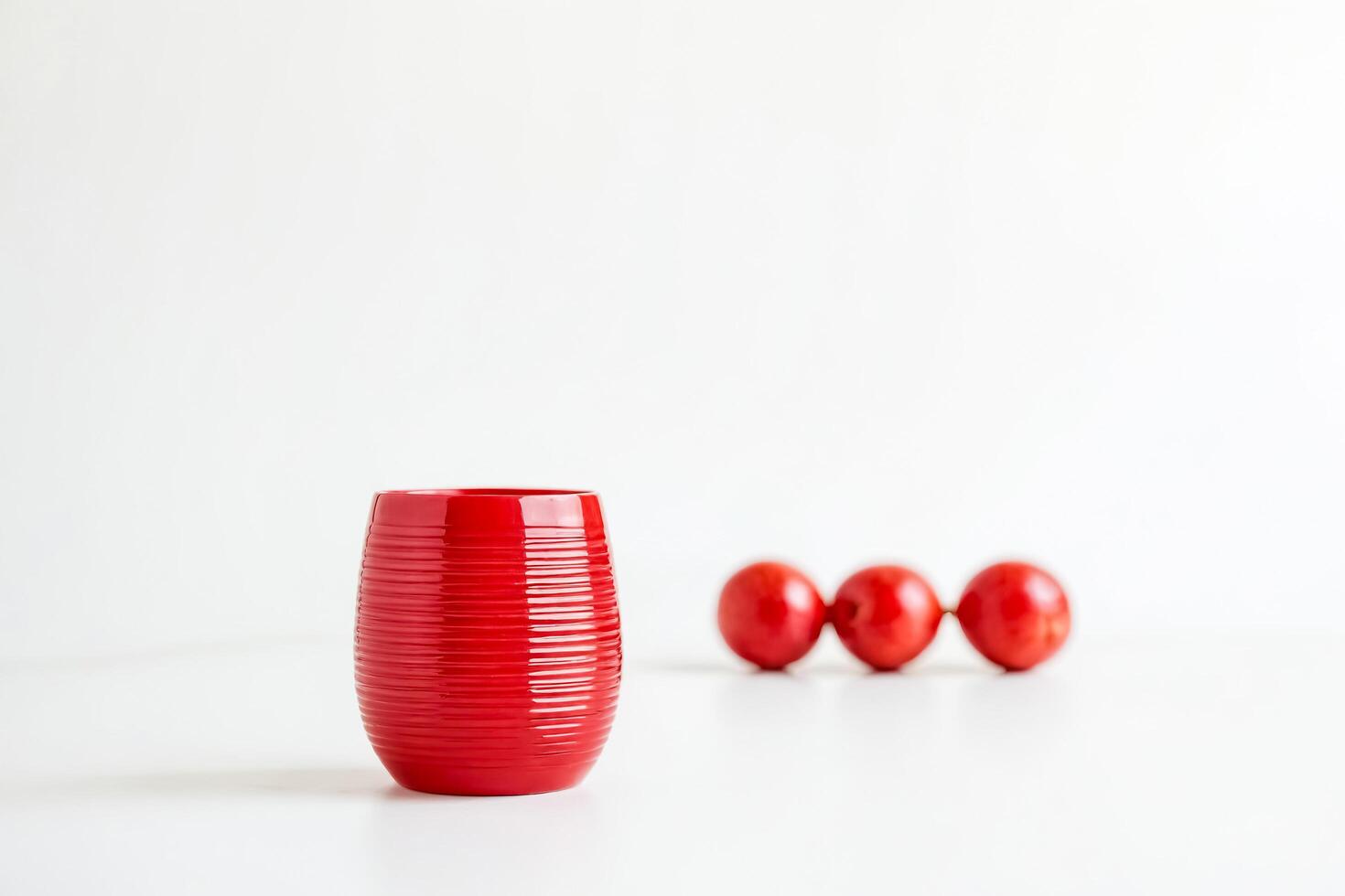 Red ceramic vase with three red round objects in the background on a white surface photo