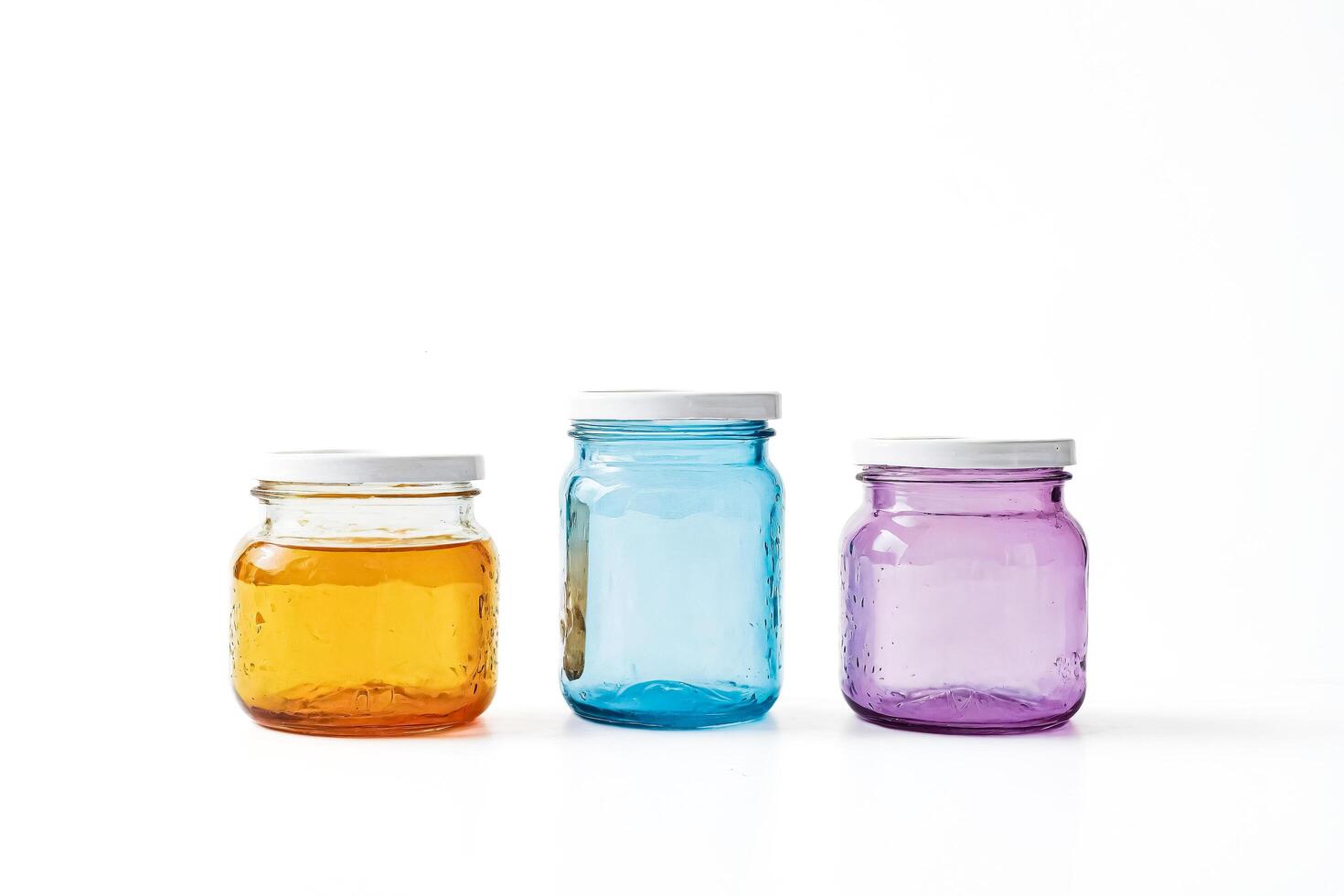 Three colorful glass jars with white lids on a white background photo
