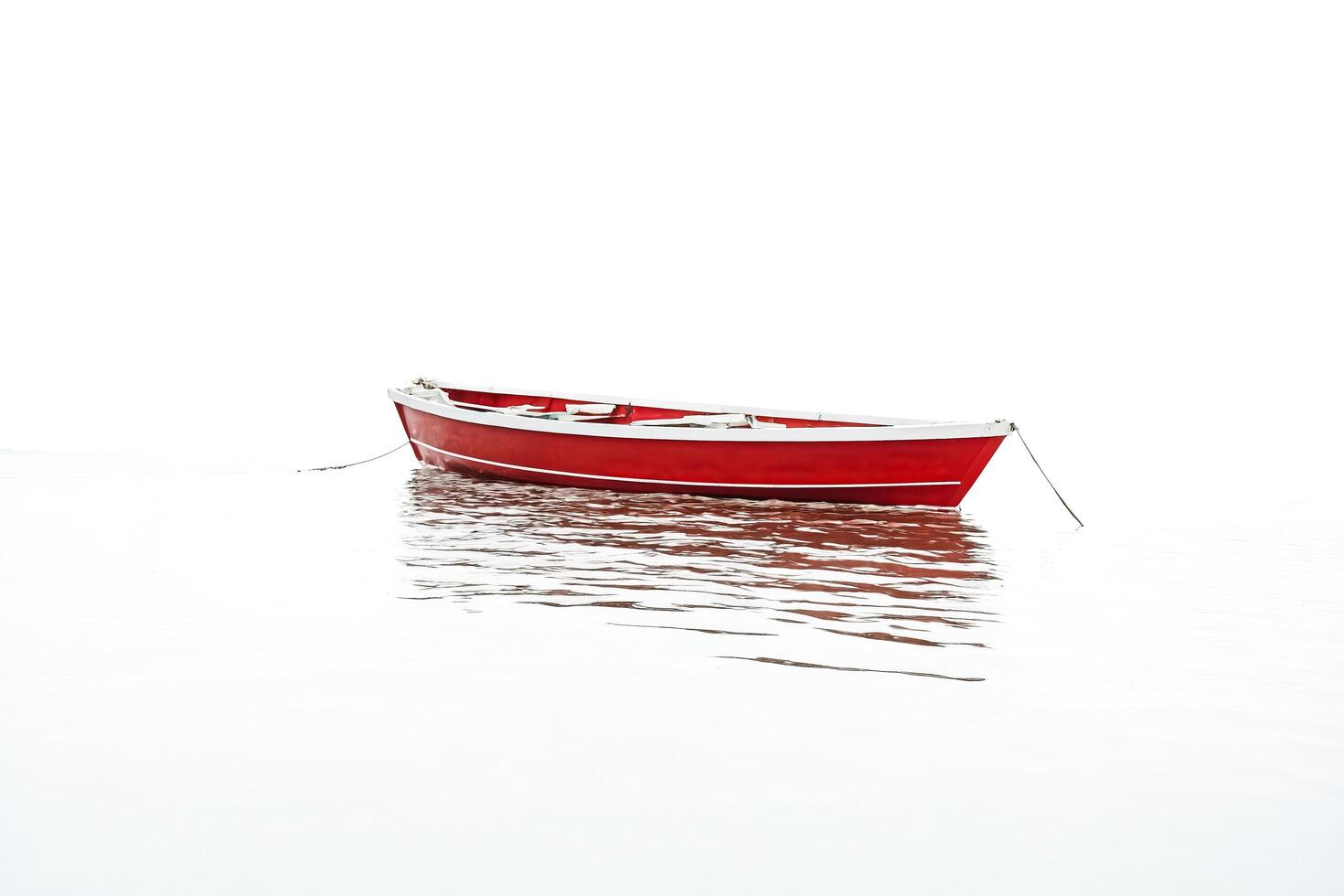 Red boat floating on calm water with white background photo