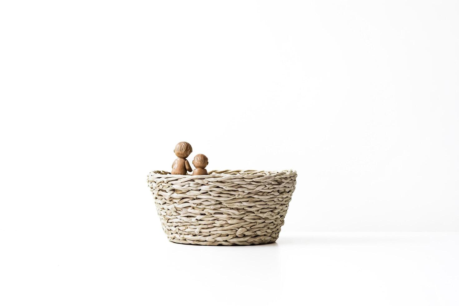Two Wooden Dolls Sitting in a Wicker Basket on a White Background photo