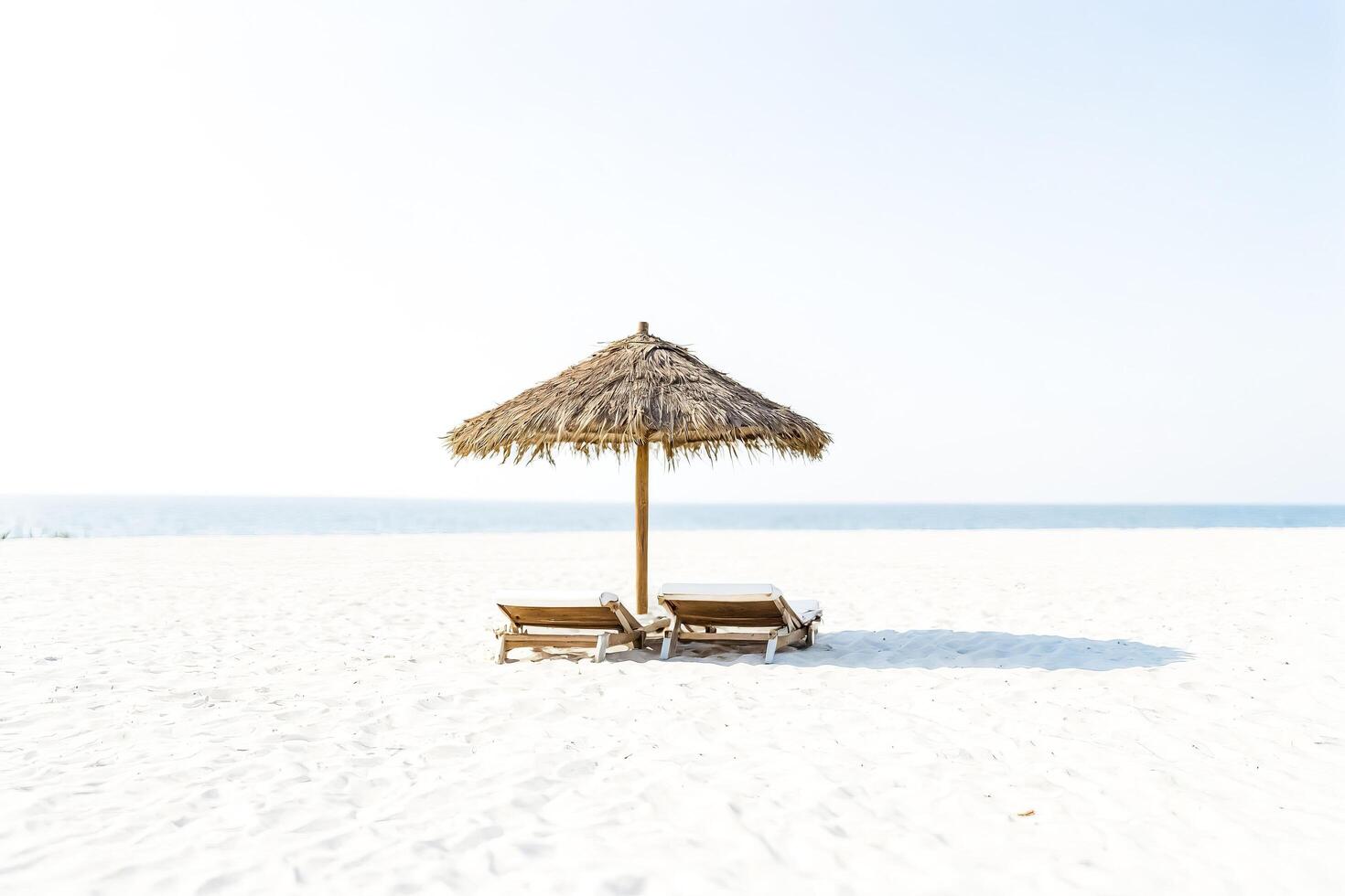Two Beach Chairs Under A Straw Umbrella On White Sand photo