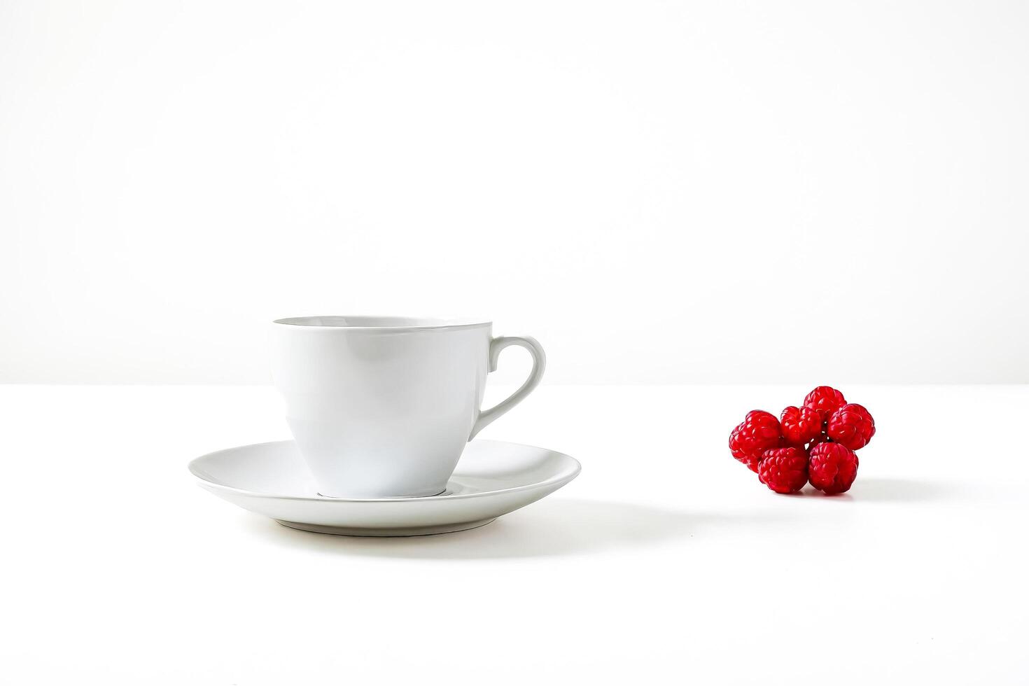 White Cup and Saucer with Red Raspberries on a White Background photo