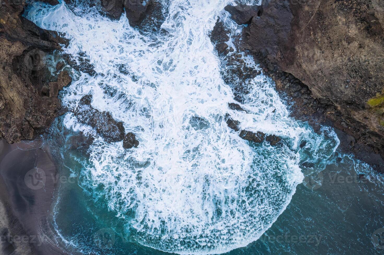 Top view of powerful crashing wave on rocky coastline photo