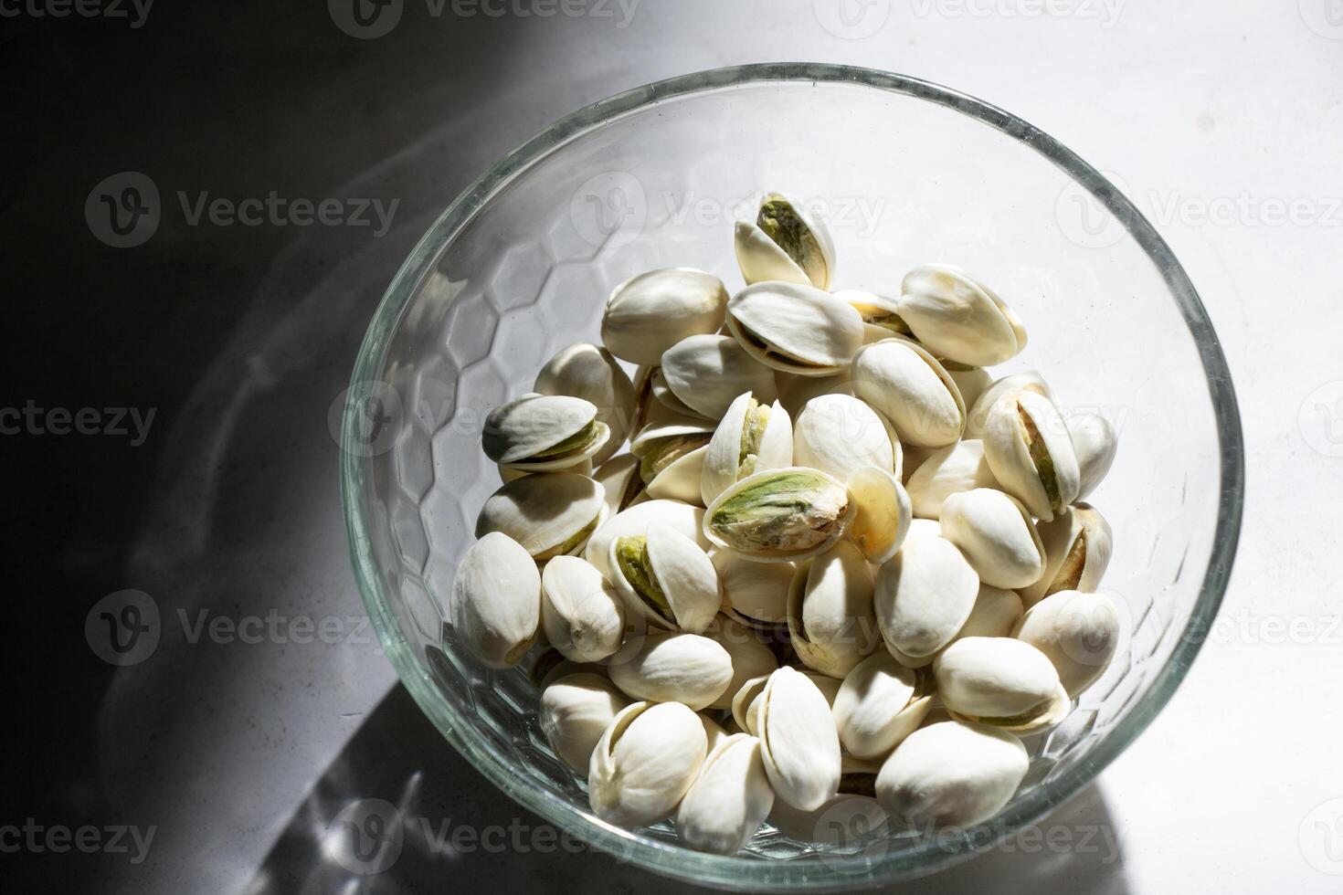 selective focus of pistachio nuts in white glass bowl isolated on light shadow shadow background, negative space photo