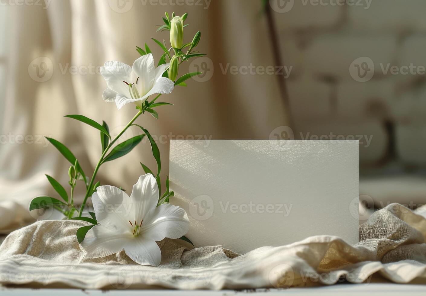 White lily with green leaves and blank card on beige fabric, illuminated by soft natural light photo