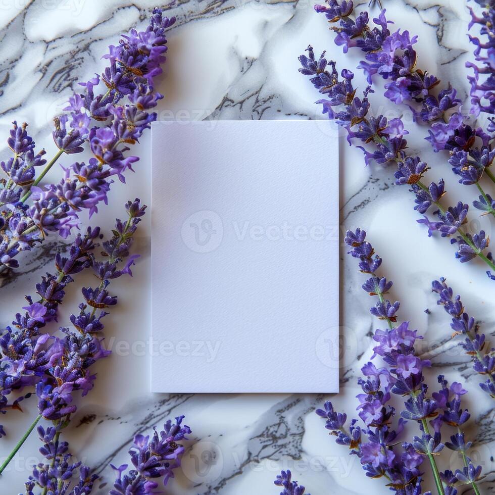 Blank white card surrounded by vibrant purple lavender flowers on a marble background, creating an elegant and minimalistic mockup perfect for invitations, greeting cards or stationery photo