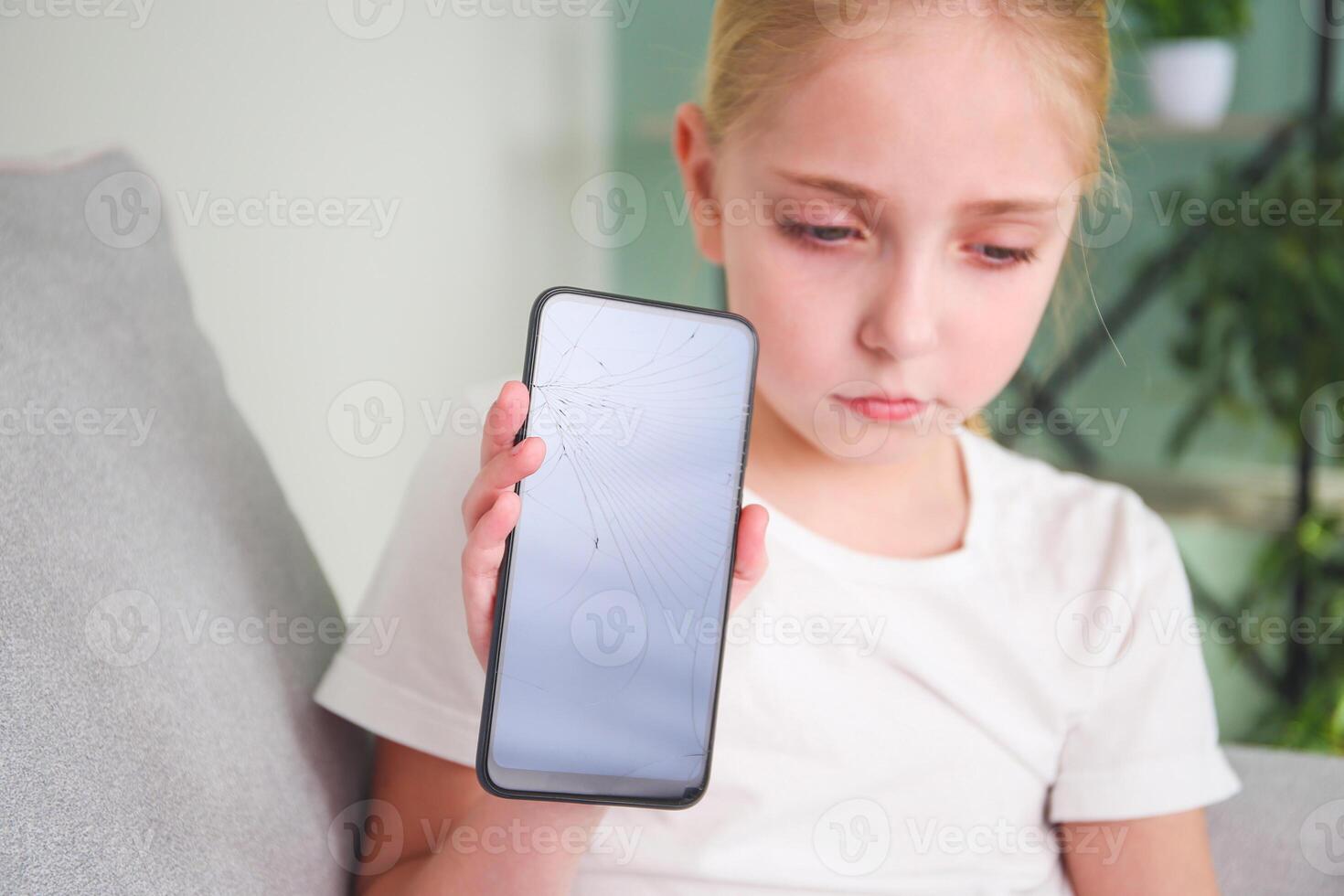 A sad girl is sitting with a broken mobile phone. The main focus is on the phone screen. Tinted image. photo