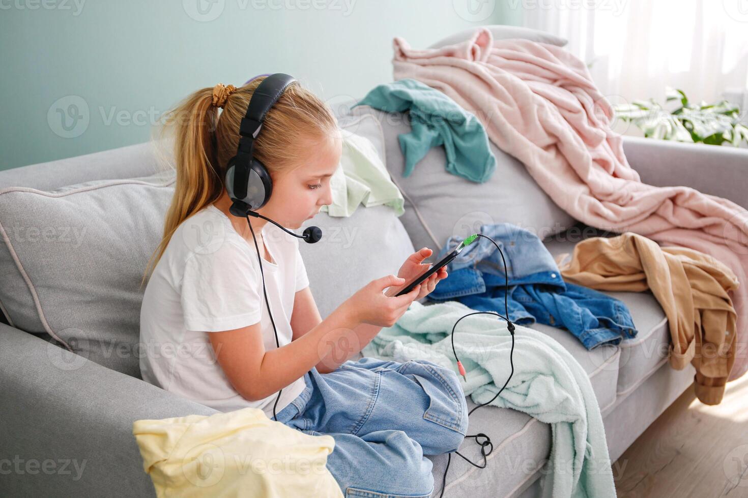 A girl is playing on a mobile phone. The room is a mess. The child scattered things in the room. photo