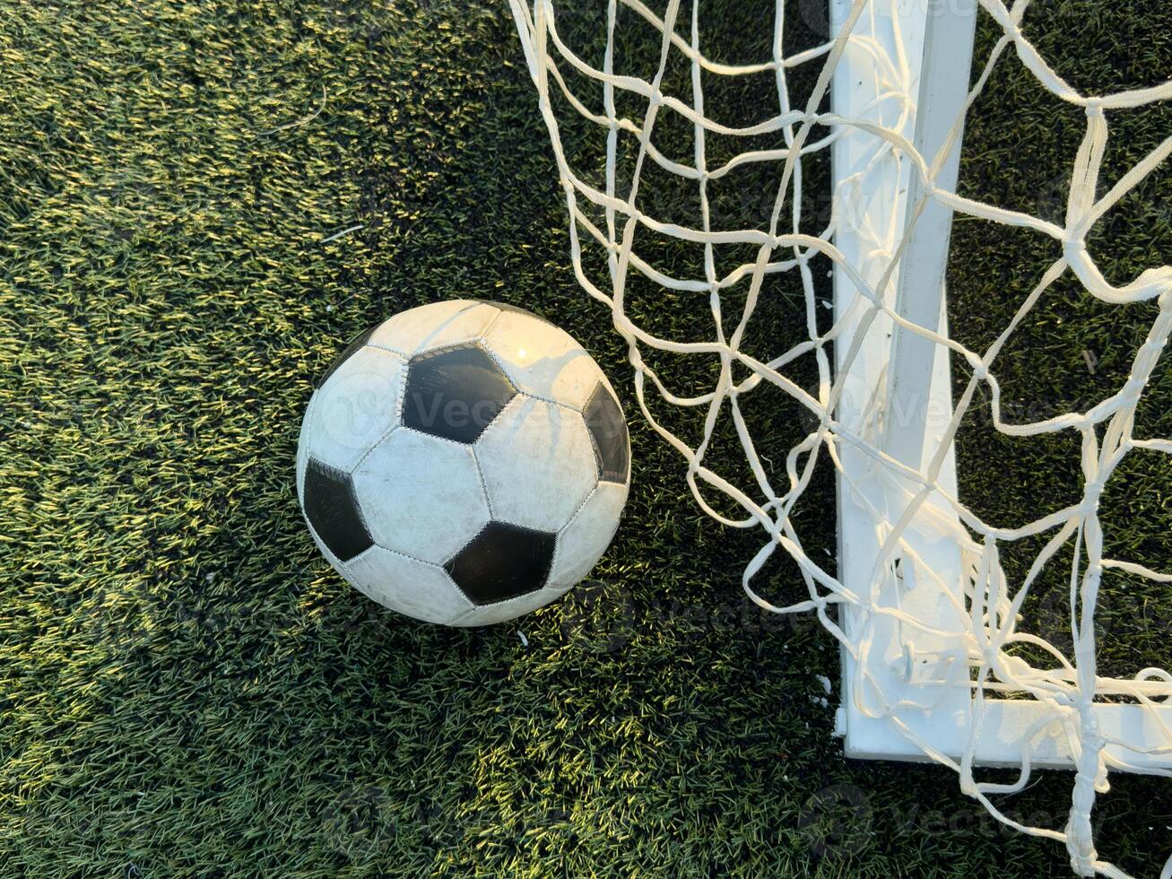 Soccer football in Goal net with green grass field. photo