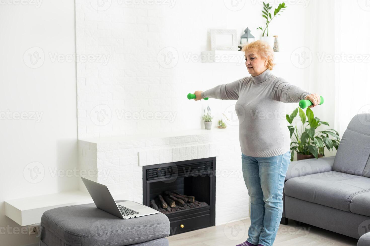 Sport In Mature Age. Happy senior woman doing stretching exercises in front of laptop at home, watching online tutorials, free space. photo