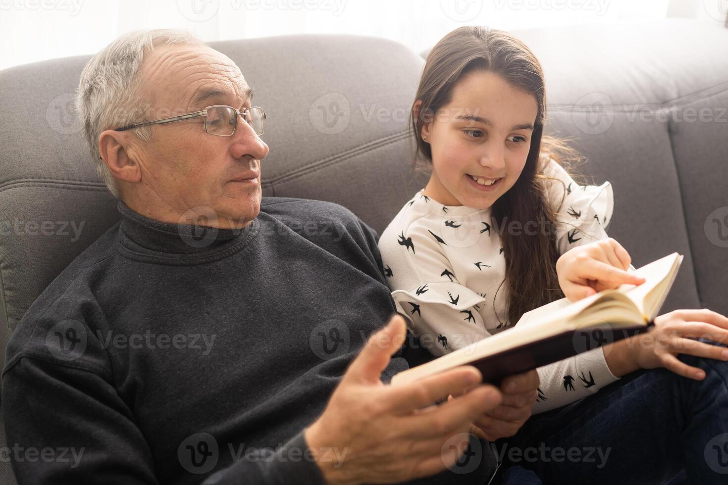 Book, family and children with a girl reading to her grandfather on the floor of their living at home. Kids, read and story with a senior man and granddaughter bonding in their house during a visit. photo