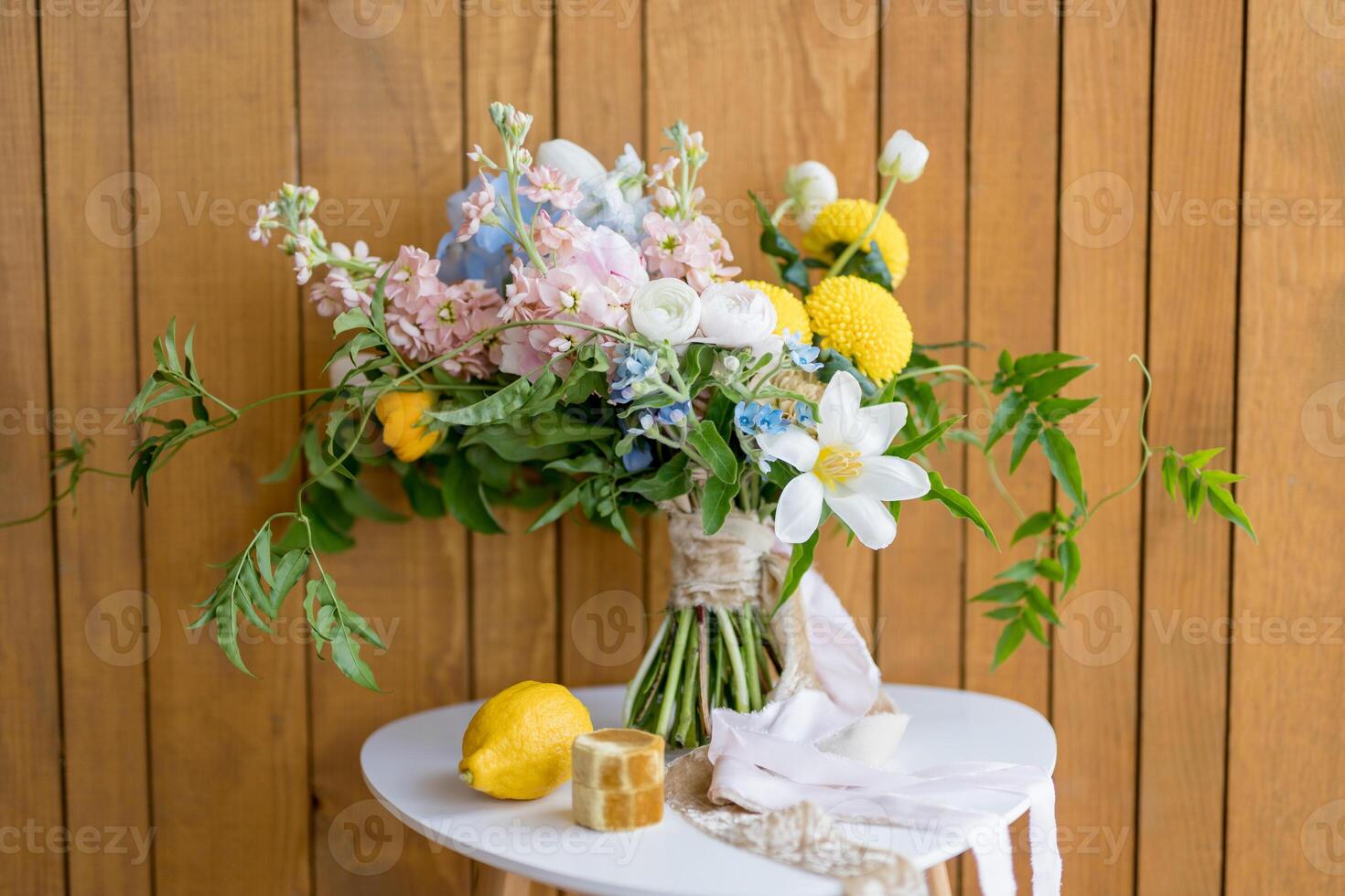 Lemon and a wooden box with rings stand next to the bride bouquet on a stool against the wall photo