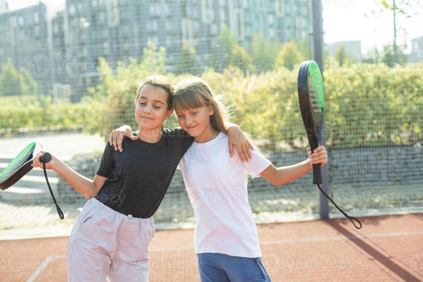 Kids and sports concept. Portrait of smiling girls posing outdoor on padel court with rackets and tennis balls photo