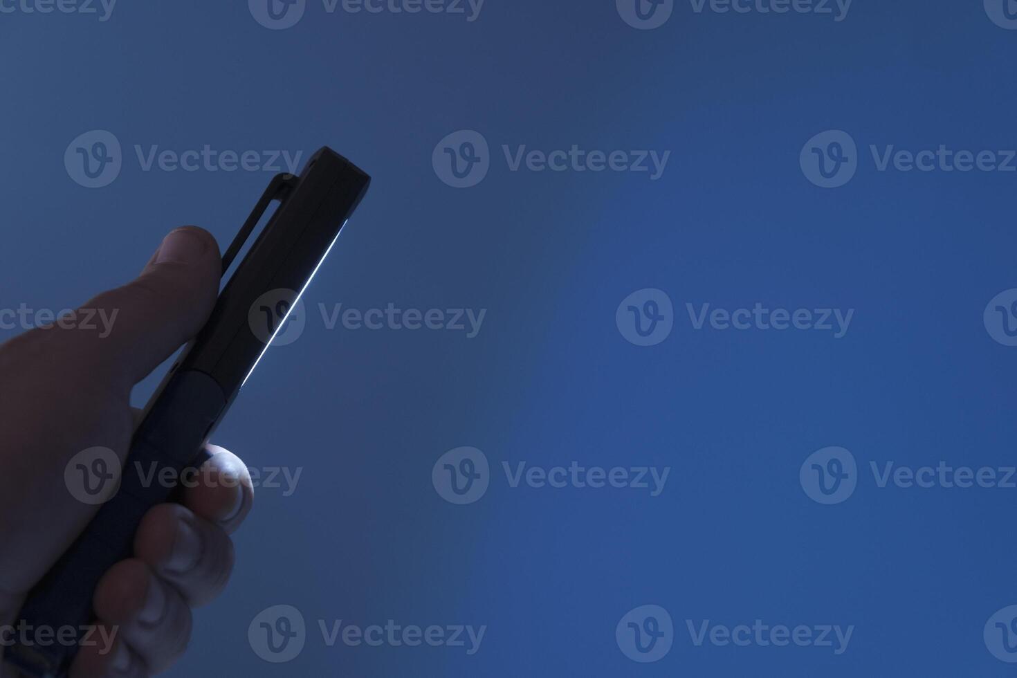 Pocket led flashlight in hand. illuminates blue background. Copy space photo