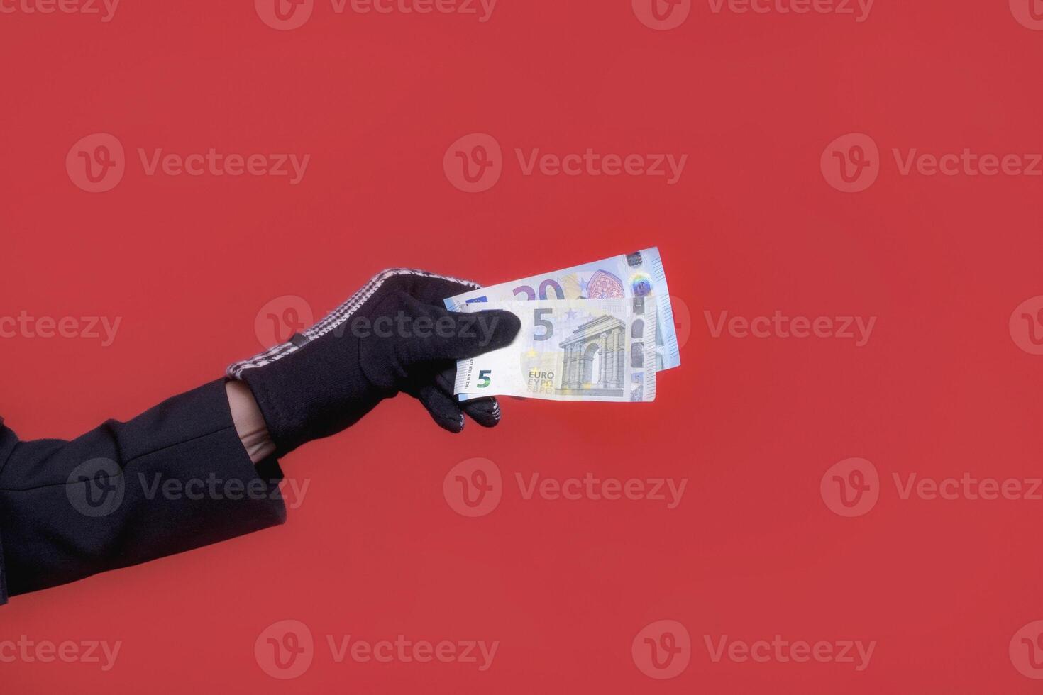 Euro banknotes in a female hand in a glove. On a red background. five and twenty euros photo