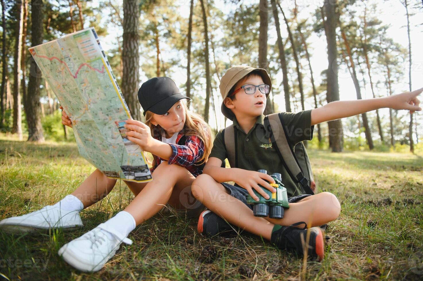 Two happy children having fun during forest hike on beautiful day in pine forest. Cute boy scout with binoculars during hiking in summer forest. Concepts of adventure, scouting and hiking tourism photo