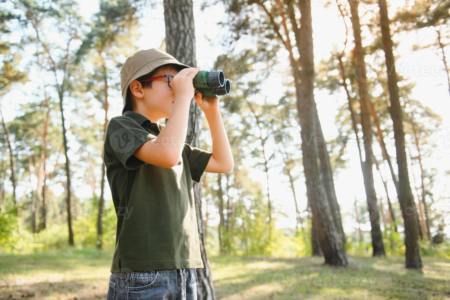 Boy with binoculars. Kid in green forest at summer daytime together. photo