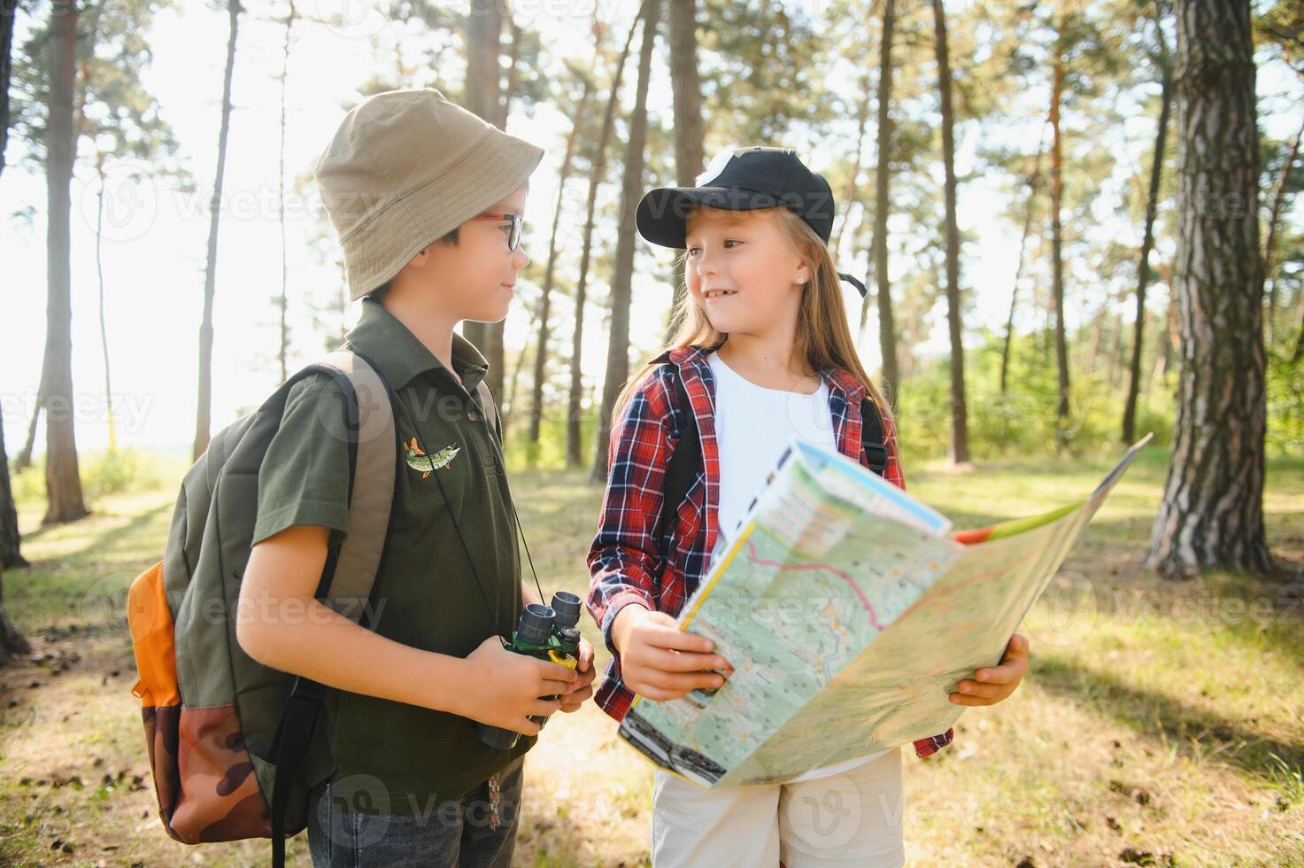 Two happy children having fun during forest hike on beautiful day in pine forest. Cute boy scout with binoculars during hiking in summer forest. Concepts of adventure, scouting and hiking tourism photo