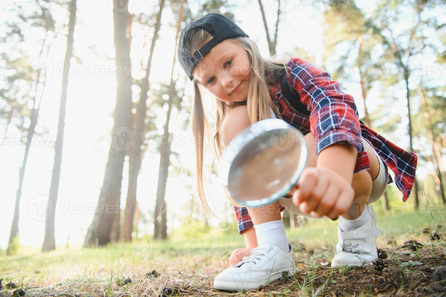 Rear view image of cute little girl exploring the nature with magnifying glass outdoor. Child playing in the forest with magnifying glass. photo