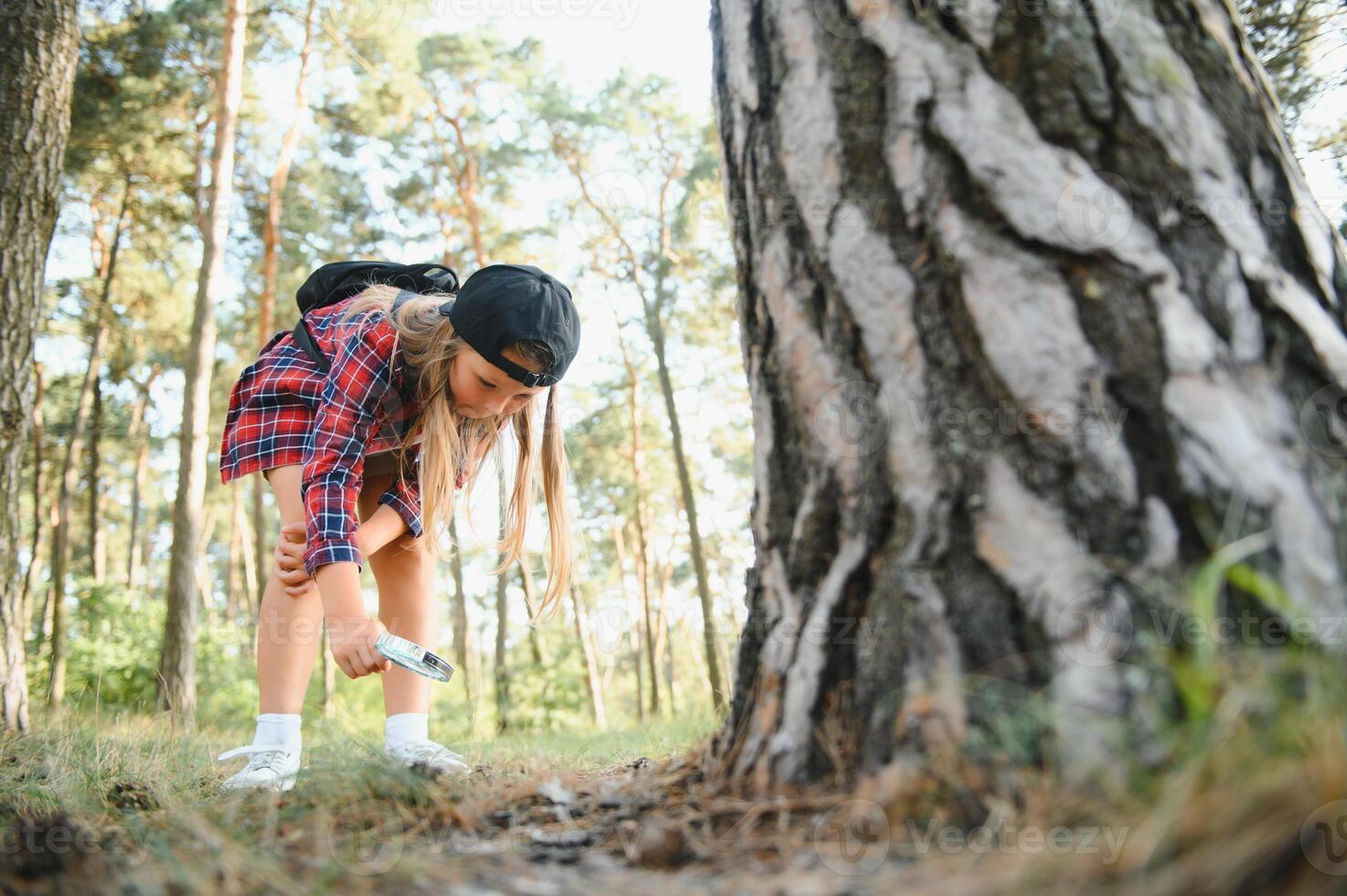 Rear view image of cute little girl exploring the nature with magnifying glass outdoor. Child playing in the forest with magnifying glass. photo