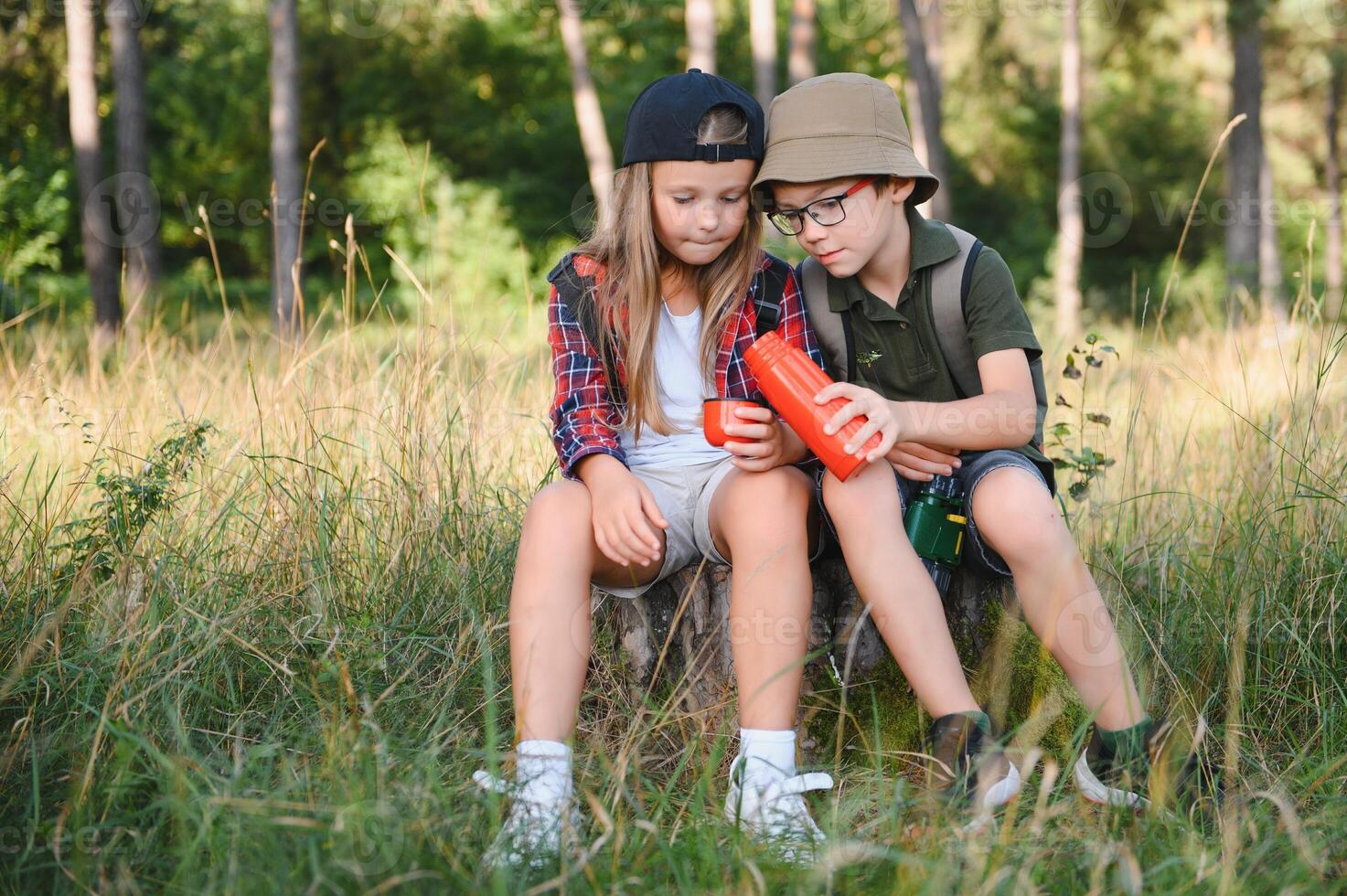 Girl and boy scout sitting and drinking hot tea from thermos in the woods photo