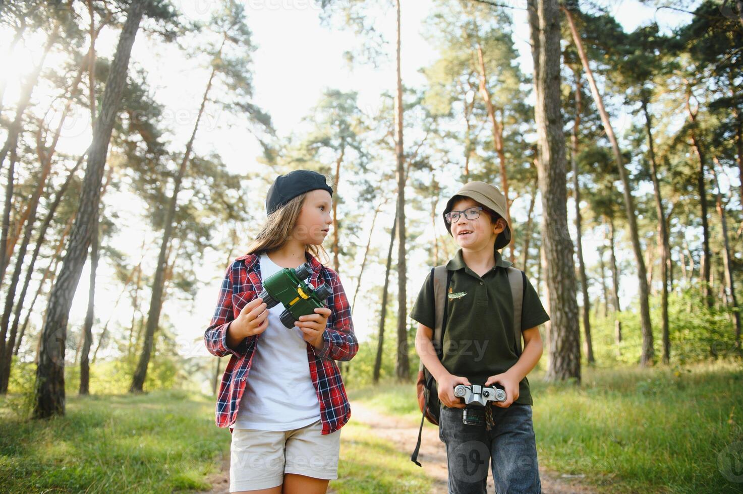 Happy excited school children with backpacks in casual clothes enjoying walk in forest on sunny autumn day, two active kids boy and girl running and playing together during camping trip in nature. photo