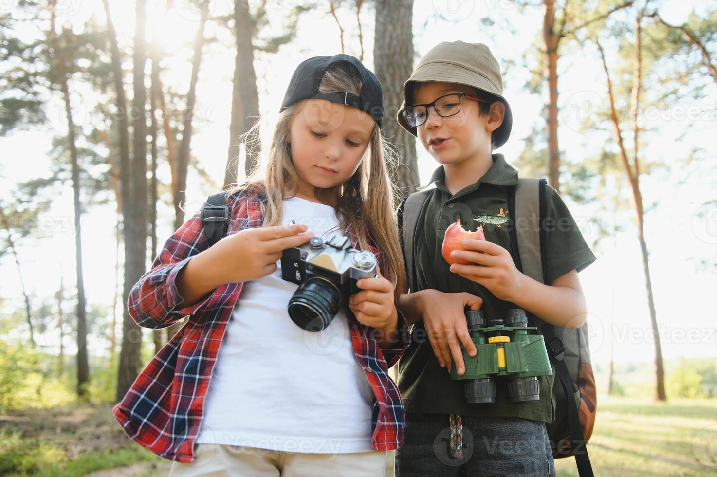 Happy excited school children with backpacks in casual clothes enjoying walk in forest on sunny autumn day, two active kids boy and girl running and playing together during camping trip in nature. photo