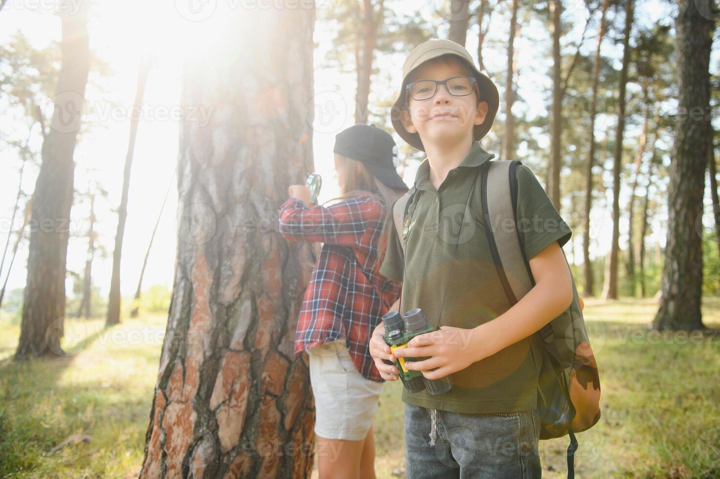 Two happy children having fun during forest hike on beautiful day in pine forest. Cute boy scout with binoculars during hiking in summer forest. Concepts of adventure, scouting and hiking tourism photo