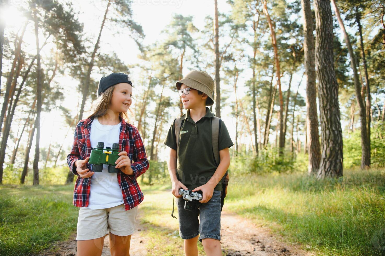 Happy excited school children with backpacks in casual clothes enjoying walk in forest on sunny autumn day, two active kids boy and girl running and playing together during camping trip in nature. photo