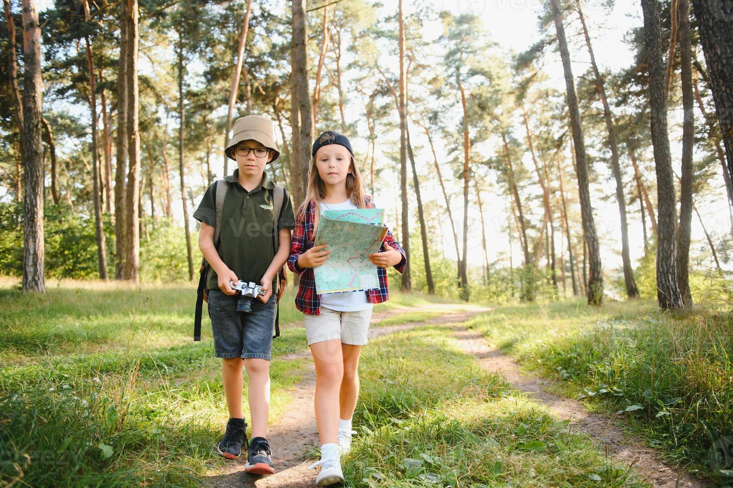 Happy excited school children with backpacks in casual clothes enjoying walk in forest on sunny autumn day, two active kids boy and girl running and playing together during camping trip in nature. photo
