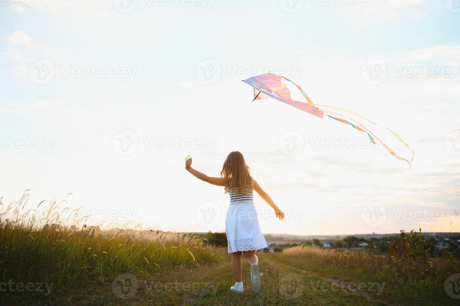 Little cute 7 years old girl running in the field with kite on summer day photo