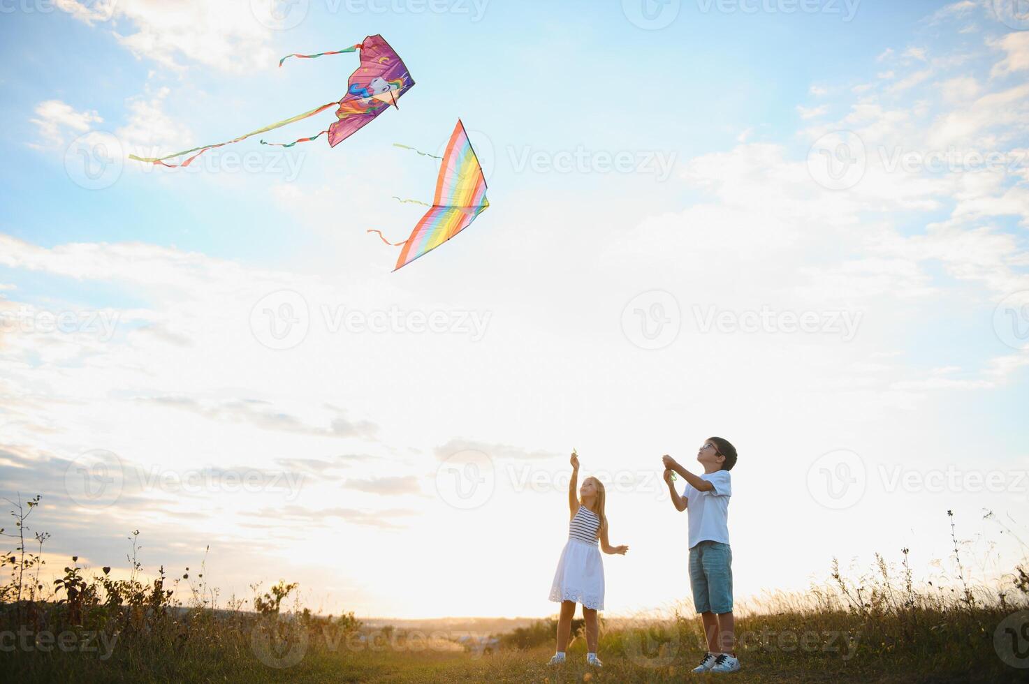 Happy children launch a kite in the field at sunset. Little boy and girl on summer vacation. photo