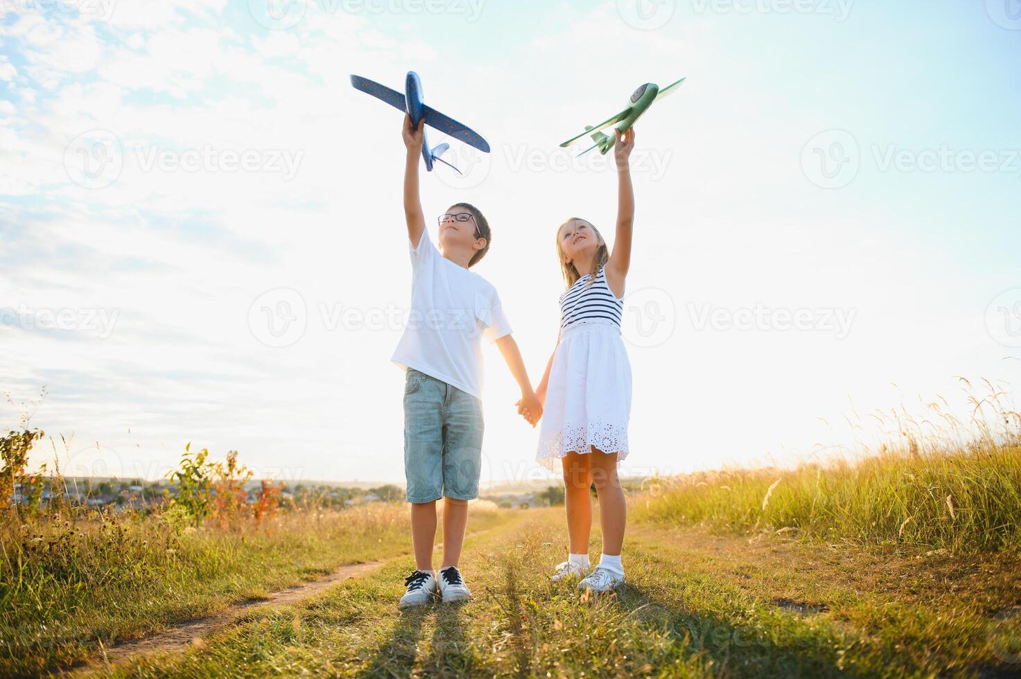 Running boy and girl holding two green and blue airplanes toy in the field during summer sunny day photo