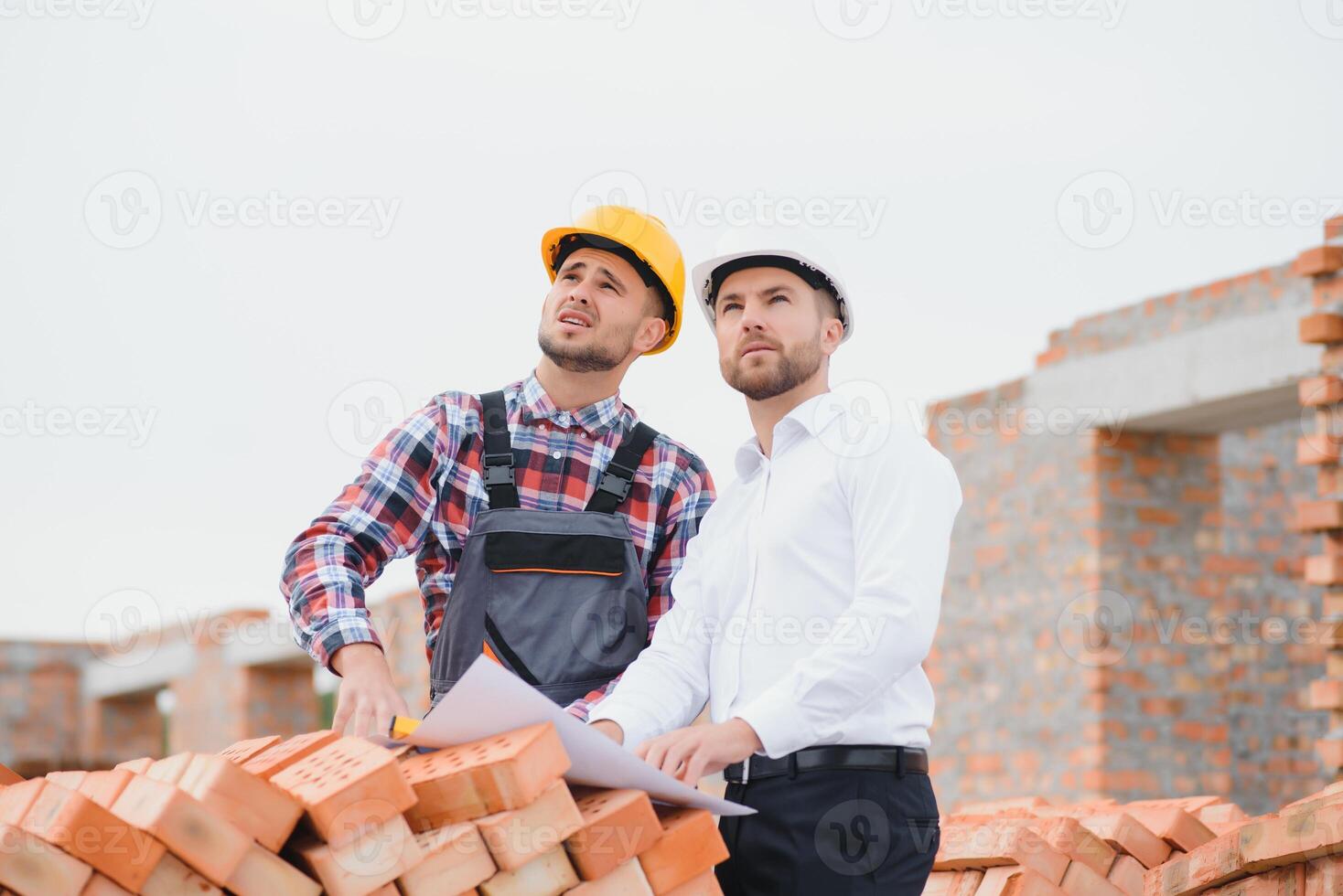engineer and builder in hard hats discussing blueprint on construction site. photo