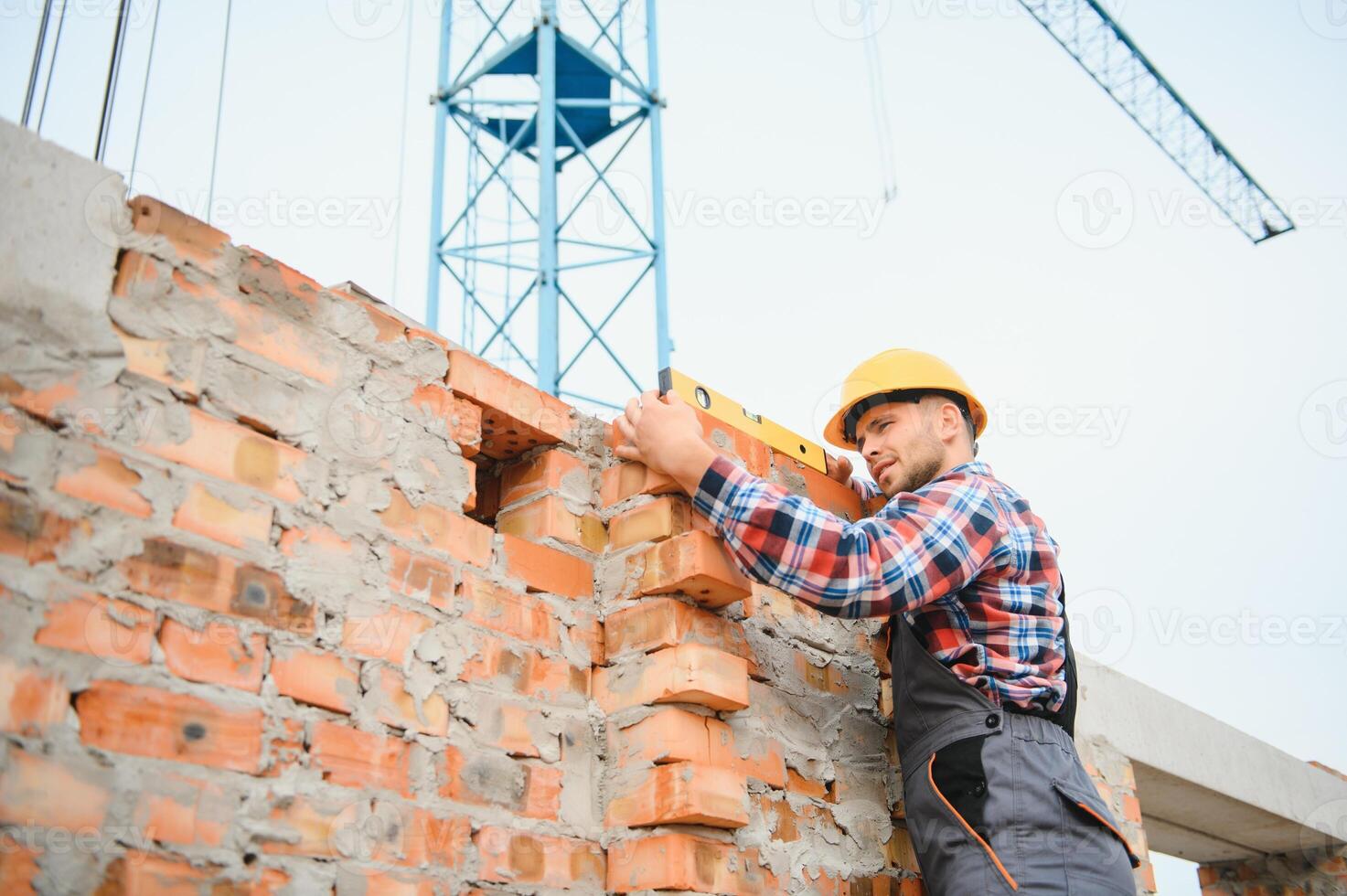 Using bricks. Young construction worker in uniform is busy at the unfinished building photo