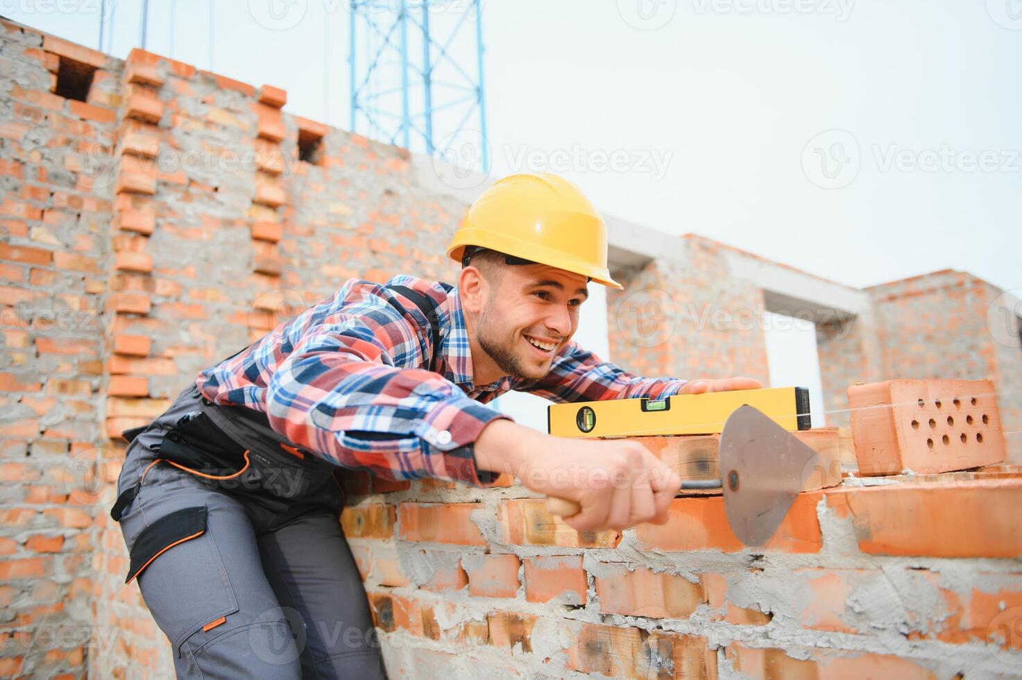 Using bricks. Young construction worker in uniform is busy at the unfinished building photo