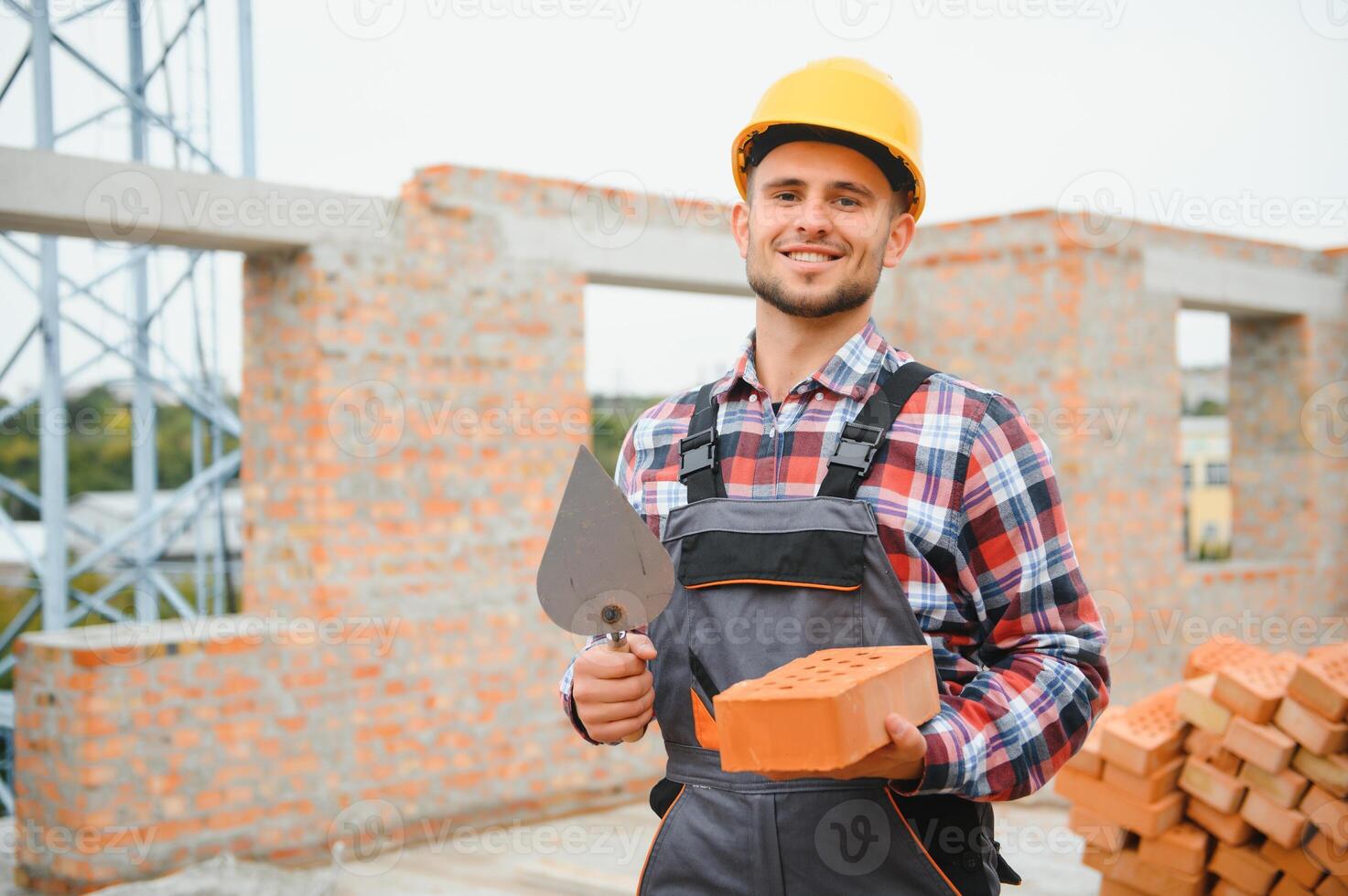 Using bricks. Young construction worker in uniform is busy at the unfinished building photo